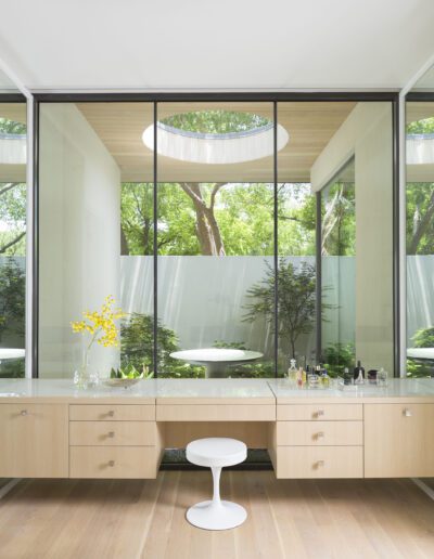 Modern bathroom with floor-to-ceiling windows overlooking a garden, featuring a floating vanity with wooden cabinetry and a circular mirror.