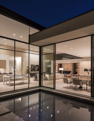 Modern home interior with large glass walls viewed from an outdoor perspective at dusk.