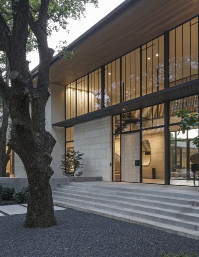 Modern building with large windows and a mix of wooden and stone facade, surrounded by trees and landscaped garden.