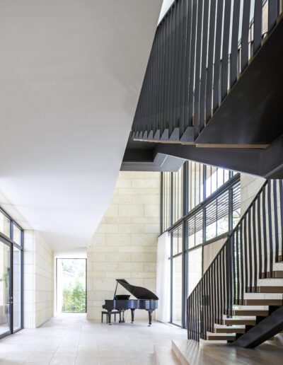 Modern interior with a grand piano near floor-to-ceiling windows and an elegant staircase with vertical balusters.