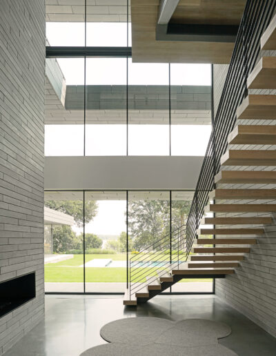 Modern interior with a floating wooden staircase, large windows, and a minimalistic design.