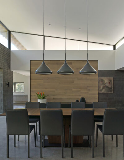 Modern dining room with a wooden table, gray chairs, pendant lights, and a fireplace.