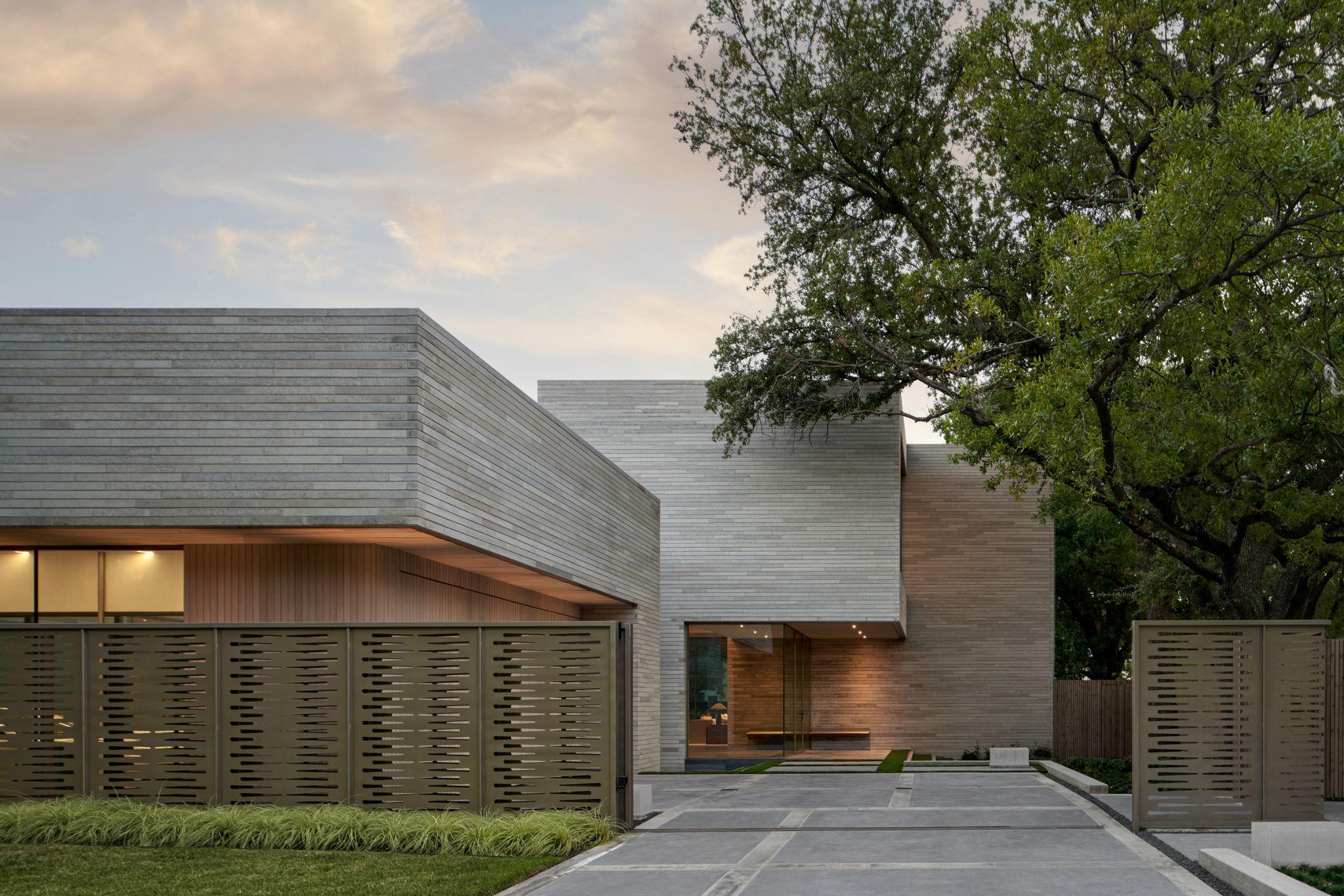 Modern building with large glass windows and a flat roof, set on a manicured lawn with trees. Pathway leads to entrance. Cloudy sky in the background.